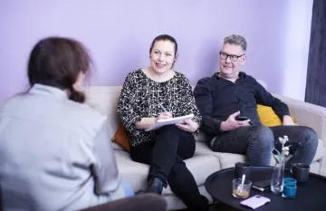 Tre personer sitter i en soffa och samtalar