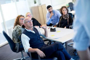 En grupp på fem personer sitter runt ett bord och lyssnar på en person som undervisar i Supported Employment och IPS